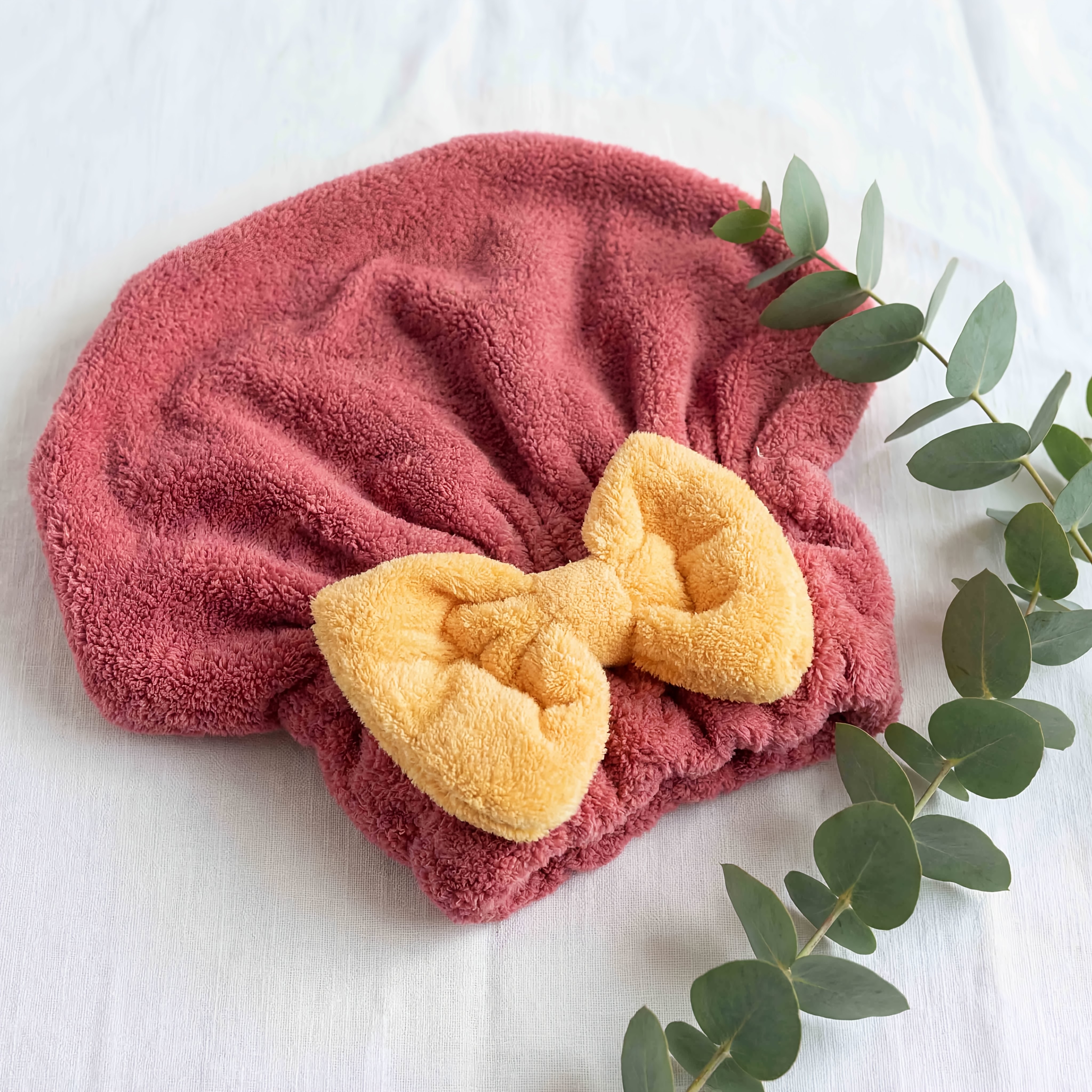 product-fancy-af5ba6ff-85ce-4d1f-878c-045233b2a883 - Boubouonaturel – Vêtements, accessoires et produits naturels Fluffy pink and orange towels with a sprig of eucalyptus resting on a light surface, captured in a flat lay arrangement.